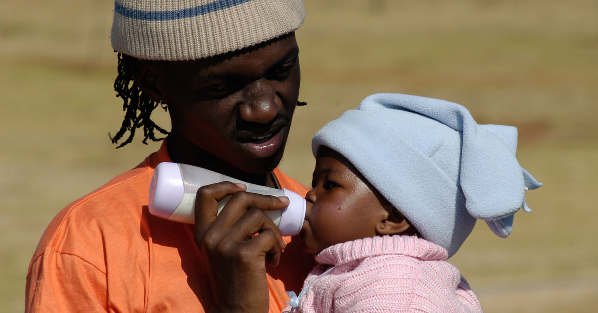 A fathers holds a baby, feeding the child with a bottle.