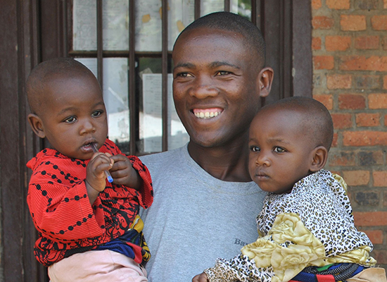 A fathers group participant in Rwanda holds his two children