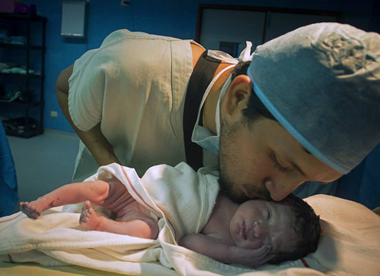 The winning photo from the MenCare Peru photography contest, a new father in scrubs kissing his newborn baby in a hospital delivery room